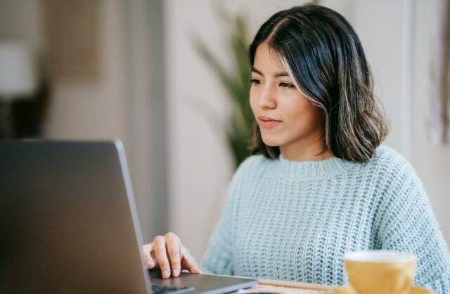 A person sitting in front of a laptop with a mug on their right.